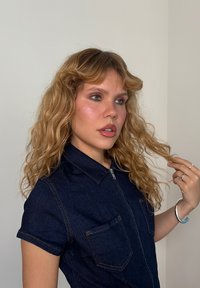 Tumman sininen farkkupaita lyhyillä hihoilla, kauluksella ja edessä vetoketjulla. Sisältää kaksi rintataskua, joissa on näkyvät ompeluyksityiskohdat.