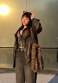 Veste en cuir marron sur un top à imprimé léopard, jean noir taille haute et sac à imprimé léopard. Lunettes de soleil noires sur la tête.