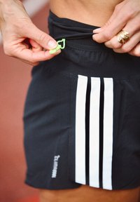 Sorte idrettsshorts med tre hvite vertikale striper på siden, med elastisk midjebånd og en grønn snor.