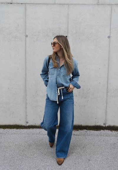 Camisa de denim y jeans de pierna ancha en diferentes tonos de azul, complementados por zapatos marrones. La camisa presenta bolsillos y un diseño de botones.