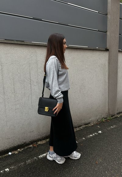 Bolso de hombro negro con herrajes dorados, sudadera gris corta, falda negra y zapatillas deportivas plateadas. Texturas suaves, diseño casual.