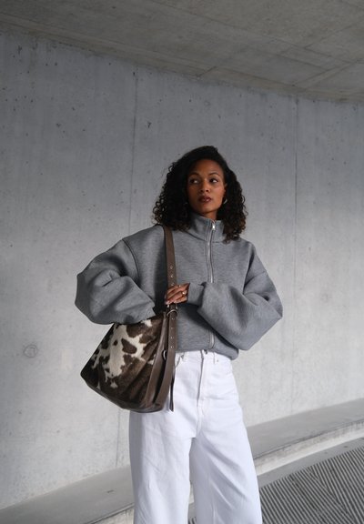 Sudadera gris con cremallera y mangas extragrandes, combinada con pantalones blancos de pierna ancha y un bolso marrón de hombro con un patrón de piel de vaca.