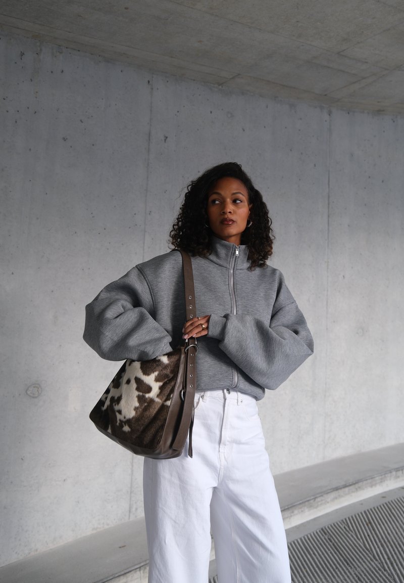 Sweatshirt cinzento com fecho de correr e mangas oversized, combinado com calças brancas de perna larga e uma bolsa castanha de ombro com padrão de pele de vaca.