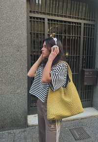 Liela dzeltena austā somiņa ar teksturētu rakstu, apvienota ar melnbaltu svītrainu atstatu topu un bēšiem sporta biksēm.