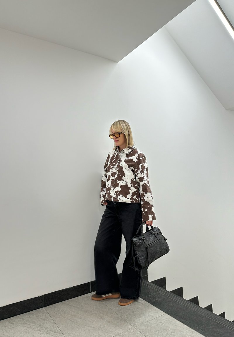 Καφέ και λευκό καρό σακάκι, μαύρα φαρδιά τζιν και μια μαύρη τσάντα. Λείες υφές, ορθογώνια γυαλιά, στέκεται σε σκάλες.