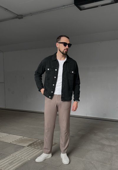 Chaqueta de denim negra, camiseta blanca, pantalones beiges y zapatillas blancas. La chaqueta tiene bolsillos frontales y botones metálicos, creando un look casual.