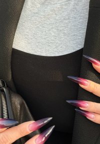 Lange, puntige nagels met een gradient van roze naar paars. Getextureerd grijze bovenkant en zwarte stof eronder, naast de rits van een zwart leren jack.