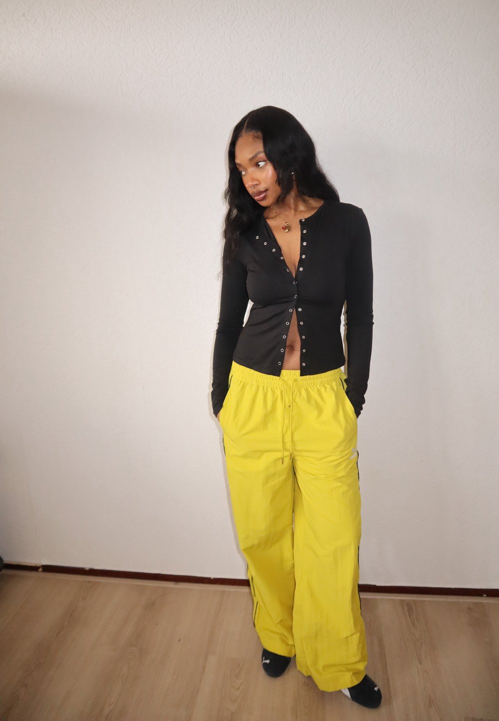 Haut noir à manches longues avec fermeture à boutons et ventre découvert, associé à un pantalon ample jaune vif avec une ceinture élastique.