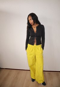 Haut noir à manches longues avec fermeture à boutons et ventre découvert, associé à un pantalon ample jaune vif avec une ceinture élastique.