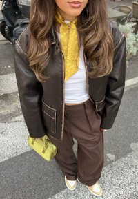 Pruun nahast lühike jope roosa äärisega, valge ribidega särk, kollane lilleline sall, pruunid laiad püksid ja väike roheline käekott.