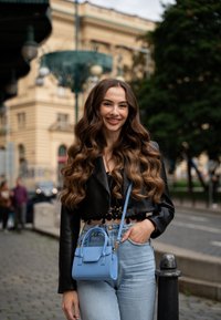 Cielo azul bolso de cuero, diseño estructurado con asas superiores y correa para el hombro, combinado con una chaqueta negra corta y vaqueros de color azul claro.