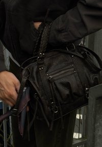 Schwarze Lederhandtasche mit geflochtenem Griff, mehreren Reißverschlusstaschen und dekorativer Hardware. Sichtbare Textur und Details heben das Design hervor.