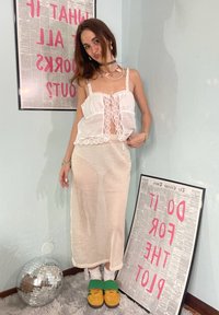 Λευκή τοπ με δαντελένιες λεπτομέρειες και διάφανη υφή, συνδυασμένη με μια διαφανή μακριά φούστα. Κίτρινες σαγιονάρες με πράσινους ιμάντες. Μπάλα disco στο προσκήνιο.