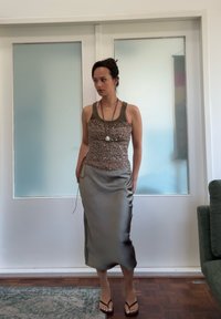 Perlebrodert brun tanktop med tynne stropper, kombinert med en skinnende, knelangs, grå satengskjørt. En enkel halskjede og flip-flops fullfører antrekket.