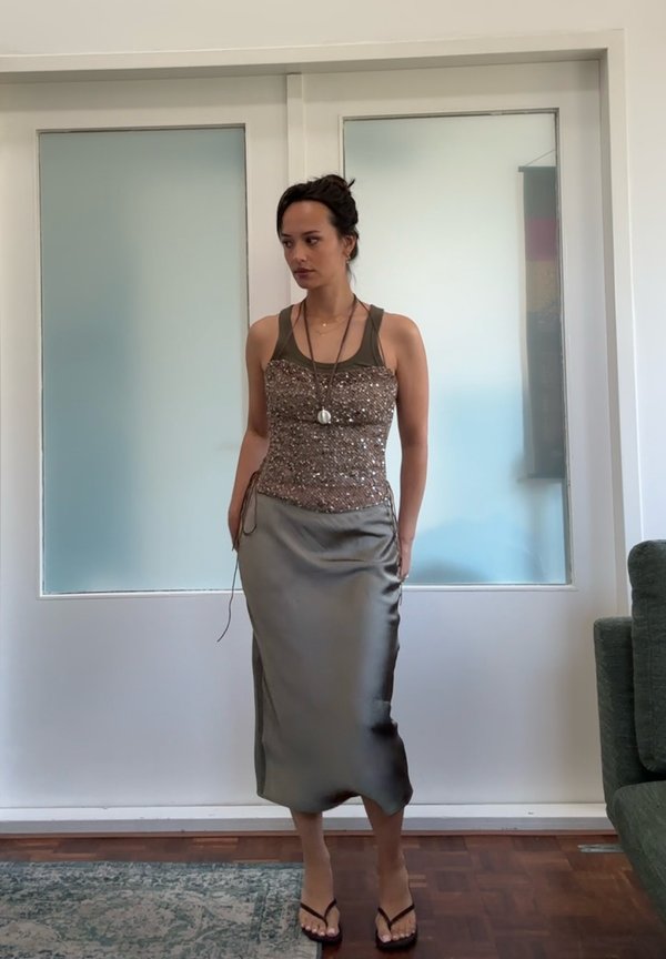Perlebrodert brun tanktop med tynne stropper, kombinert med en skinnende, knelangs, grå satengskjørt. En enkel halskjede og flip-flops fullfører antrekket.