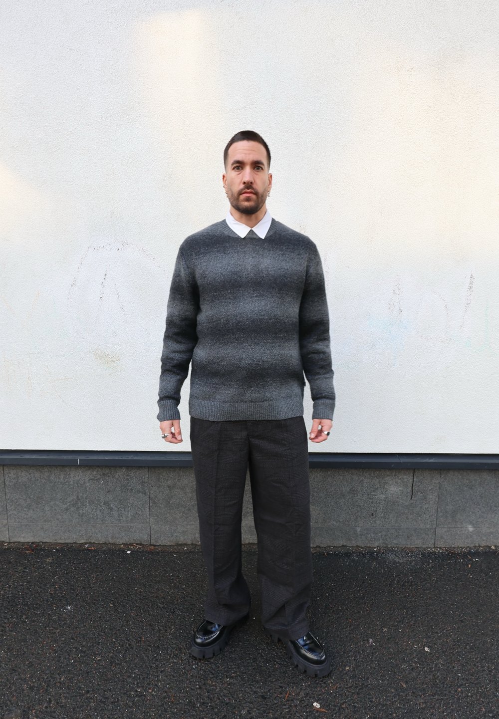 Pull rayé gris avec un ourlet côtelé, chemise blanche à col dessous, et pantalon ample texturé foncé. Chaussures à plateforme noires.