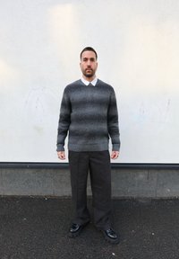 Pull rayé gris avec un ourlet côtelé, chemise blanche à col dessous, et pantalon ample texturé foncé. Chaussures à plateforme noires.