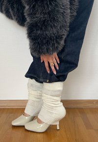 Beliče bele nogavice, prekrivajoče temno denim, v kombinaciji s sijočimi bež petami. Teksturni, puhasti plašč in vidna kovinska prstan.