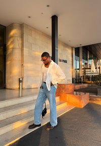 Vabaaja riietus, mis koosneb valgest linast särgist, valgest toppist, helesinistest teksapükstest ja pruuni värvi jalanõudest, koos musta üleõlakoti ja võtmehoidjaga.