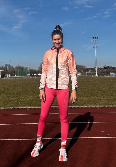 Chaqueta con capucha de color rosa claro con cremallera frontal, combinada con leggins rosas ajustados y calcetines de rayas coloridas, llevada con zapatillas deportivas blancas.