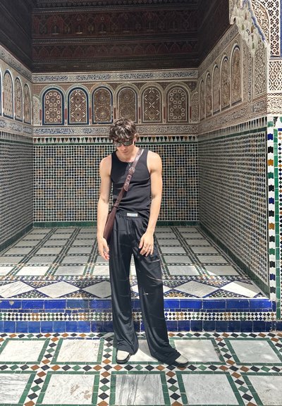 Top negro sin mangas, pantalones negros holgados y un bolso marrón de hombro. Patrón de azulejos intrincado con formas geométricas en verde, azul y blanco.