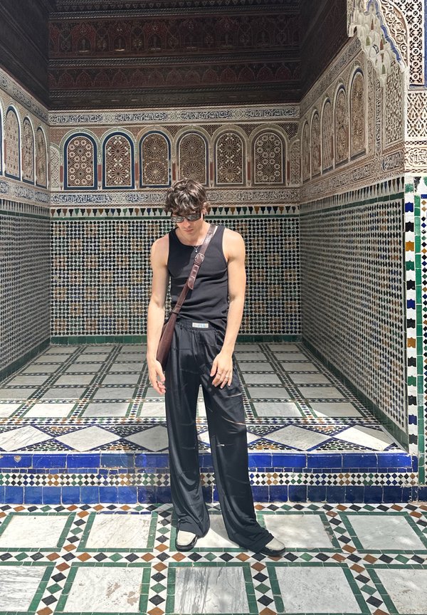 Top preto de alças, calças pretas largas e uma bolsa de ombro castanha. Padrão de azulejos intrincado com formas geométricas em verde, azul e branco.