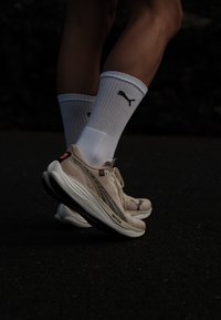 Beige sport schoenen met zwarte accenten en een textuur van mesh aan de bovenkant, gecombineerd met witte kniekousen met een zwart logo.