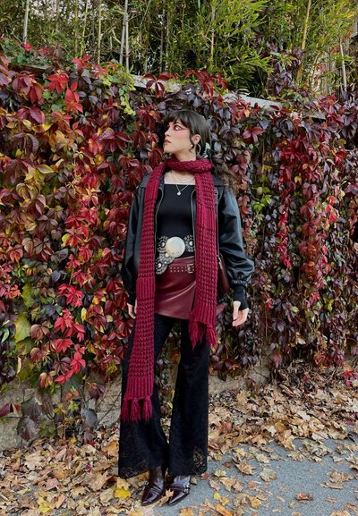 Chaqueta de cuero negra, bufanda de lana marrón, camiseta negra ajustada, falda de cuero sintético burdeos, pantalones de encaje negros acampanados, botas tobilleras marrones brillantes.