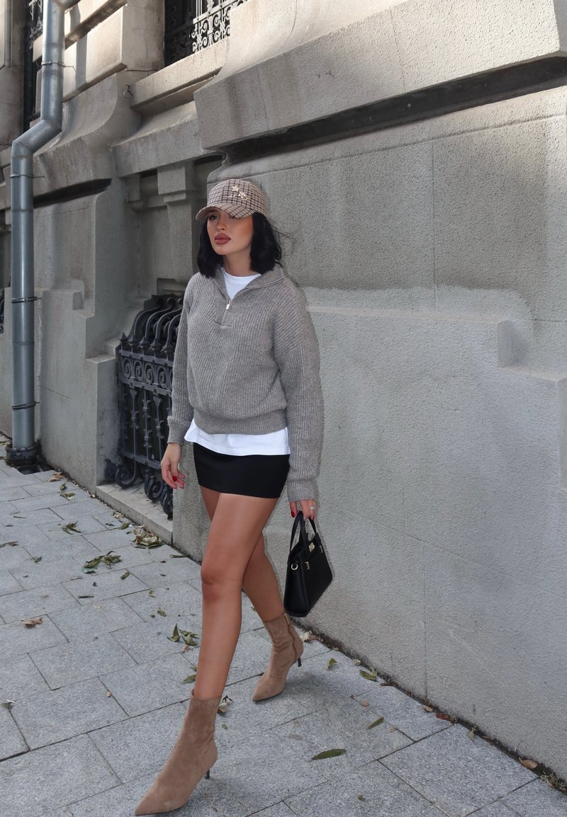 Pull en tricot gris clair, T-shirt blanc en dessous, mini-jupe noire, bottines en daim beige à la cheville, portant un petit sac à main noir, à l'extérieur.