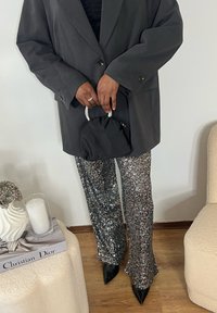 Sort oversized blazer over en tætsiddende top, kombineret med sølvglitrende, udvidede bukser og spidse sorte hæle. Holder en lille sort taske.