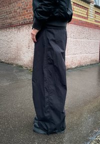 Svarte vide bukser i et lett, vannavstøtende stoff med en glatt tekstur, kombinert med svarte robuste ankelstøvler.