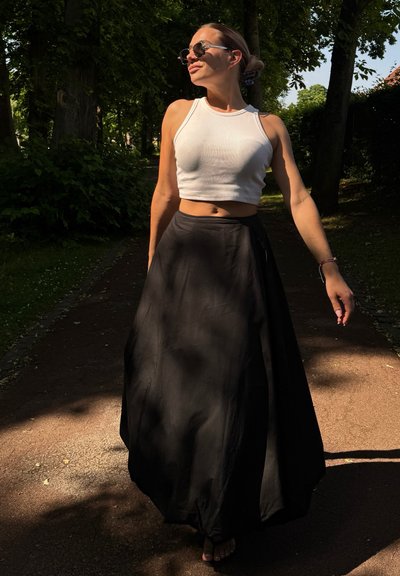 Top corto blanco, falda maxi negra fluida, llevada con gafas de sol. El atuendo presenta una textura suave y un corsé ajustado con una silueta suelta.