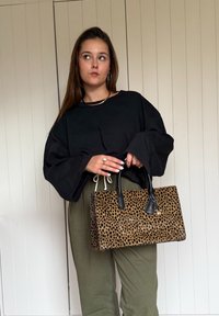 Tasje met luipaardprint en zwarte handvatten, rechthoekige vorm en textuur oppervlak. Gecombineerd met een zwarte top en groene broek.