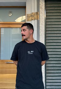 Zwarte T-shirt met korte mouwen met daarop de witte logo-tekst "FFFF" aan de voorkant. Eenvoudig ontwerp met een relaxed fit, staand tegen een textuur achtergrond.