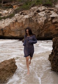 Rochie vaporoasă, cu dungi, de culoare bleumarin, cu mâneci lungi, care ajunge până la mijlocul coapsei, purtată de o persoană care merge desculță în apă puțin adâncă.