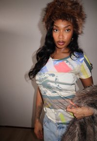 T-shirt à manches courtes à imprimé graphique avec des couleurs vives et des motifs tropicaux. Associé à un chapeau en fourrure brune duveteuse et un jean en denim.