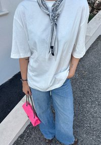 T-shirt branca oversized com um bolso, combinada com jeans de perna larga em azul claro. Uma bolsa rosa com alças de corrente e um lenço estampado estão incluídos.