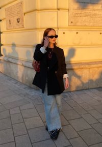 Μαύρο σακάκι με διπλό κούμπωμα πάνω από μαύρο crop top, ανοιχτού γαλάζιου παντελόνι με φαρδιά πόδια και μαύρα παπούτσια. Τα αξεσουάρ περιλαμβάνουν γυαλιά ηλίου και καφέ τσάντα.