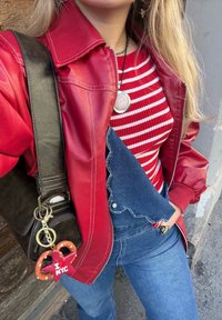 Red leather jacket, striped red and white top, blue denim overalls, and a black bag featuring a pretzel keychain. A casual outfit with layered textures.