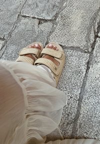 Bež sandale s dva široka pletena remena, podesivim čičak trakama i glatkim potplatima, uparenim s laganom, teksturiranom tkaninom.
