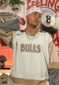 Jersey Nike w białym kolorze z beżowymi i szarymi akcentami; posiada logo „BULLS” w wyrazistym kroju; teksturowana tkanina i luźny krój. Akcesoria w postaci łańcuchów i bandany.