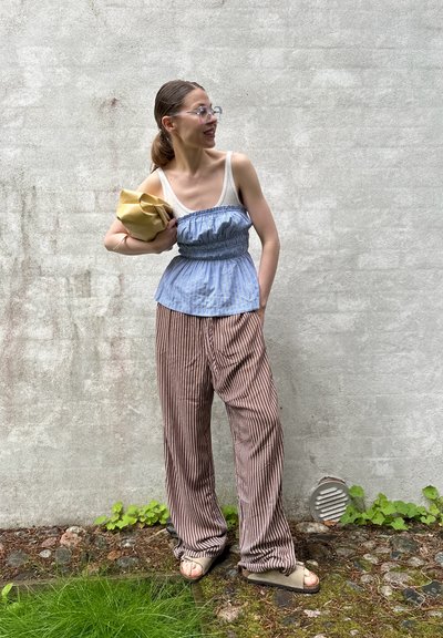 Top peplum a rayas azul y blancas, cintura elástica; pantalones de pierna ancha a rayas marrones y blancas; calzado minimalista; sosteniendo un bolso amarillo.