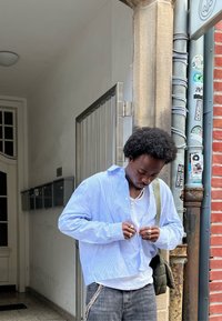 Ανοιχτό μπλε, ριγέ πουκάμισο με κουμπιά, χαλαρή εφαρμογή, φορεμένο πάνω από λευκό t-shirt; συνδυασμένο με γκρι τζιν και τσάντα μέσης.