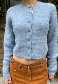 Lys blå, fluffy cardigan med lange ermer og knapper foran; kombinert med rustfargede bukser med et dekorativt belte.