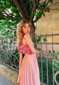 Robe plissée rose avec un design de corsage floral rouge. Le tissu est lisse, avec une silhouette fluide et un détail en ruban à l'arrière.