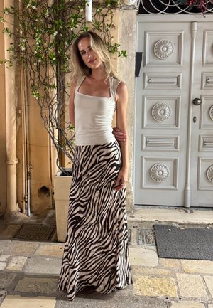 Camiseta sin mangas en tejido blanco combinada con una falda larga y ajustada con un estampado de rayas de cebra en negro y beige. Escenario al aire libre con una puerta decorativa.