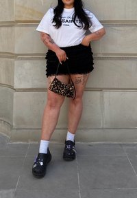 Bela majica s tekstom "SAINTS LONDON", črna nabrana mini krila, torba z leopardjim vzorcem ter črne okrašene obuvala z belimi nogavicami.