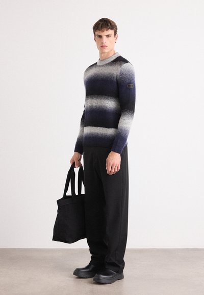 Suéter de punto con rayas en navy, gris y blanco, cuello redondo, mangas largas, combinado con pantalones negros y un bolso tote negro.