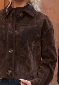 Pruun seemisnahast jakk krae, hõbedaste nööpide ja lühikese lõikega. Tekstuuriga pind ja nähtavad õmblused annavad sellele rohkem iseloomu.