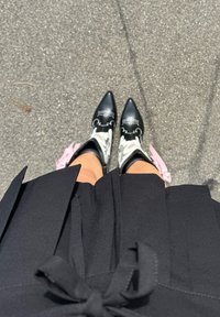 Svarte spisse cowboy-boots med hvitt og rosa blomstermønster, side detaljer, brukt med et svart antrekk med en sløyfade.